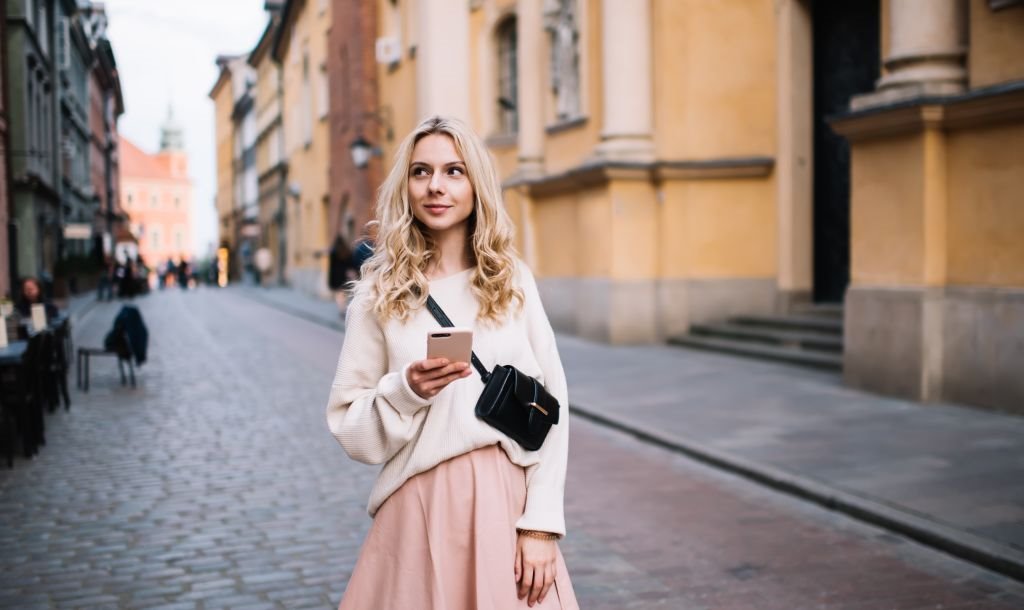 Devojka šeta ulicom sa telefonom u ruci.